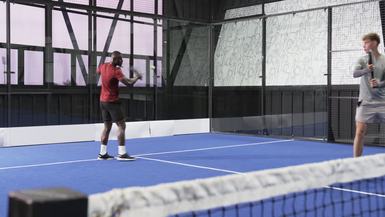 Two diverse men playing padel tennis on indoor court, enjoying competitive match
