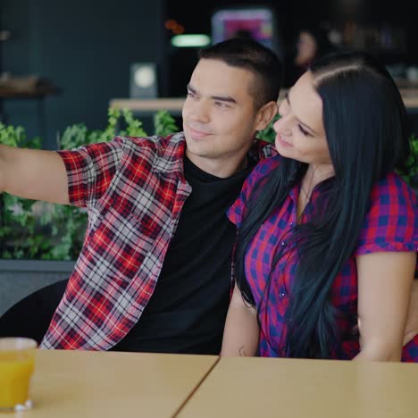 beautiful couple in plaid shirts are sitting at the table and taking selfies. dating in the cafe