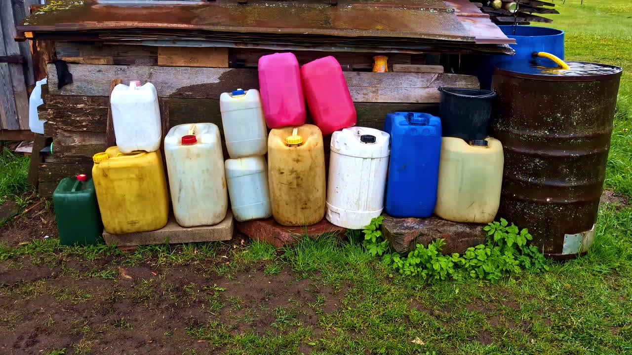 Colorful collection of plastic jerry cans and barrels stored beside weathered shed