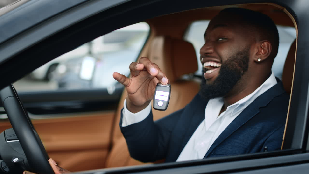 Closeup businessman shaking key in new car. African man smiling in vehicle