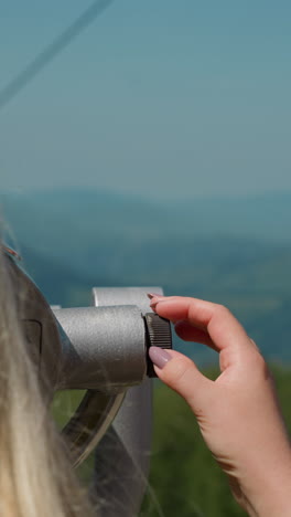 blonde lady turns wheel to adjust tower viewer and enjoy landscape with mountains from view point at resort close backside view slow motion