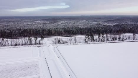 aerial view over snow covered field and road with parked car near massive forest