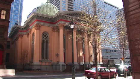 un maravilloso edificio antiguo con un colorido exterior naranja y una cúpula verde pálido que contrasta con los rascacielos de vidrio y acero que lo rodean