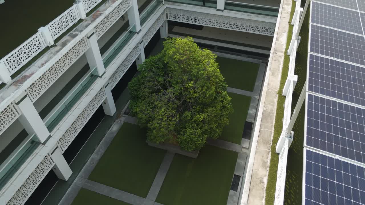 A close-up drone shot of solar panels on the rooftop of the Raja Haji Fi Sabililah Mosque in Cyberjaya, Malaysia, with a view of a courtyard and a tree