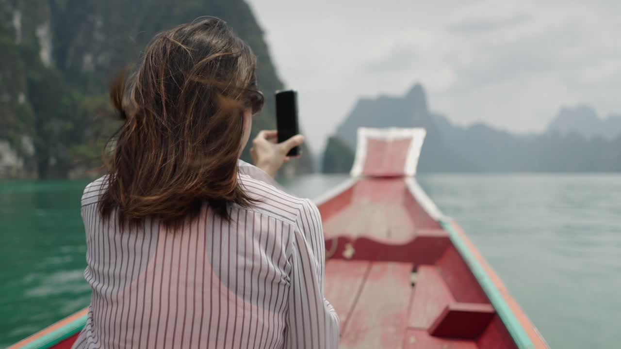 Woman taking photos of scenic lake and mountains from a boat