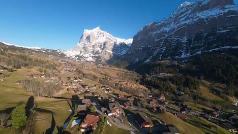 Homes-in-valley-with-steep-cliff-faces-of-Swiss-Alps-and-snow-covered-peaks-in-distance