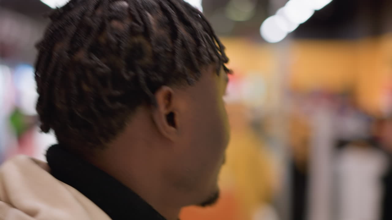 young black man with dreadlocks in hoodie and turtleneck looking at bokeh boutique interior lighting exploring modern retail environment thoughtful shopper portrait side profile close up