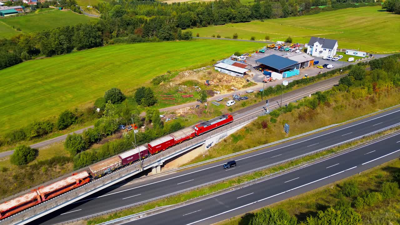Freight Train with Red Locomotive Crossing Bridge Over Highway in Countryside Landscape