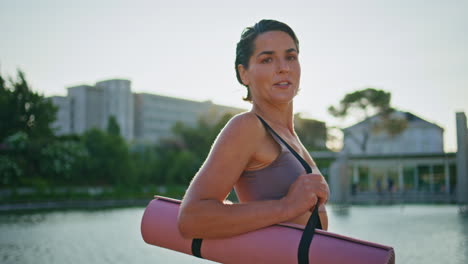 feliz yogini posando en el terraplén del lago retrato de la mañana. mujer deportiva mirando la cámara