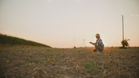 agricultora inspeccionando el suelo en un campo al atardecer