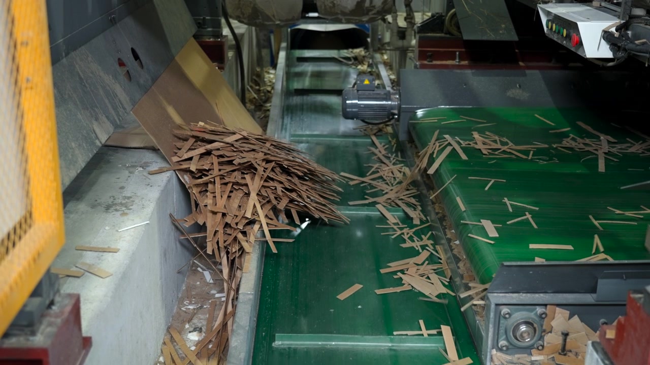 Close up industrial processing line shows wooden slats and scraps shifting across green conveyor belts inside factory machinery, with industrial, factory, machinery, conveyor detail