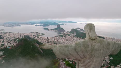 aerial view dolly in passing by the side of christ the redeemer towards rio de janeiro, brazil on a cloudy day