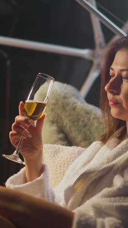 woman with contemplative gaze sits in chair fixating on glass of alcoholic elixir. woman remains motionless lost in own world captivated by spirituous liquid