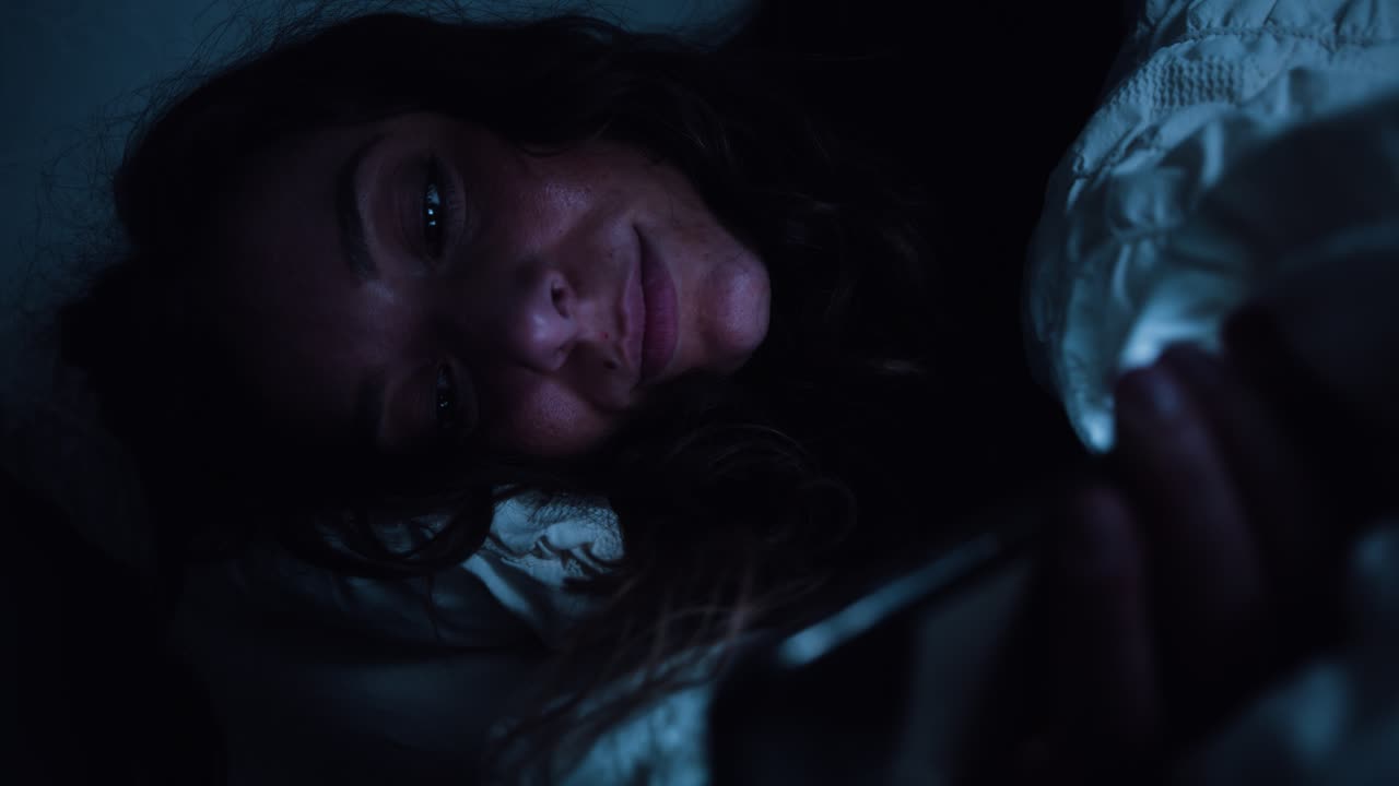 女性がベッドに横たわっている間スマートフォンを使用しています