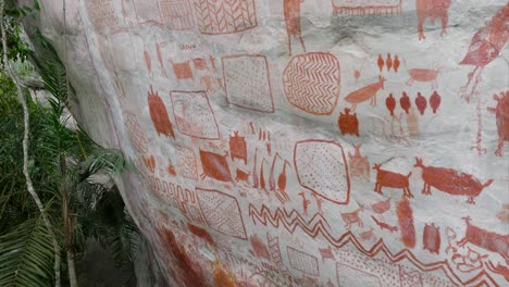 ascending drone shot of a cliff showing many ancient paintings