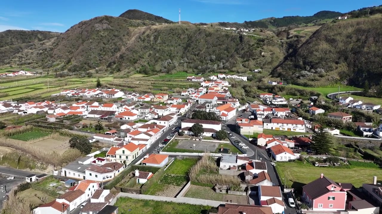 Ampio panorama aereo del villaggio costiero di Mosteiros, incastonato tra le montagne e l'Oceano Atlantico, con rocce vulcaniche e tradizionali case bianche sulla costa dell'isola di São Miguel, Azzorre
