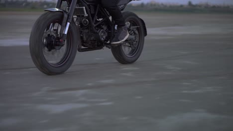 close up of biker's ride on black sport bike by sandy ground in evening dusk