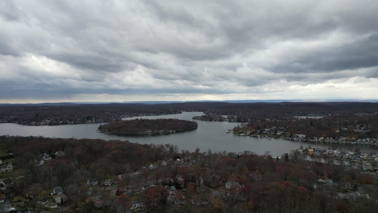 Low altitude drone flight over Larchmont’s lakeside showing a bay with houses, piers, and rich autumn foliage. Dramatic cloudy skies reflect on the water. Ideal for real estate or location B-roll