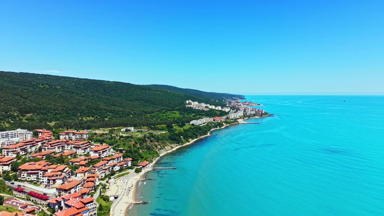 Yazın güneşli bir günde, berrak mavi sulara sahip bir sahil kasabasının deniz kenarı manzarası.