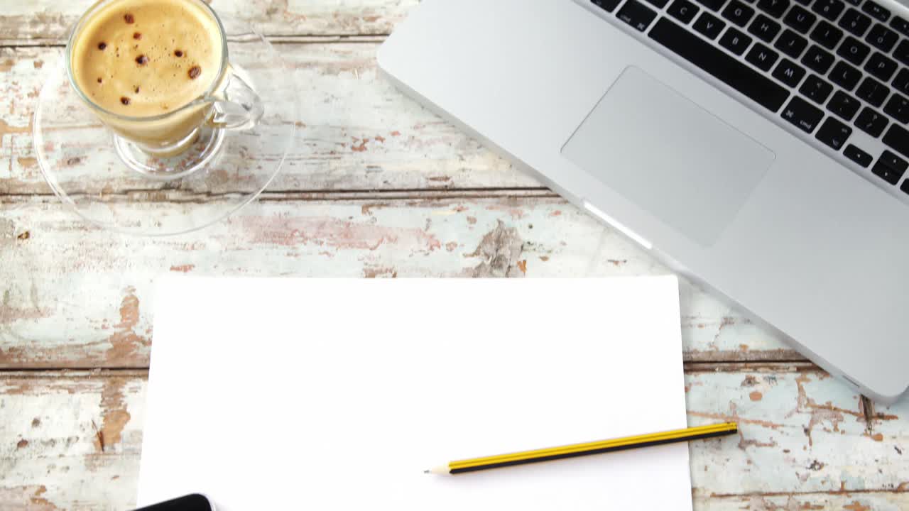 taza de café, portátil, teléfono móvil, papel, lápiz en una tabla de madera