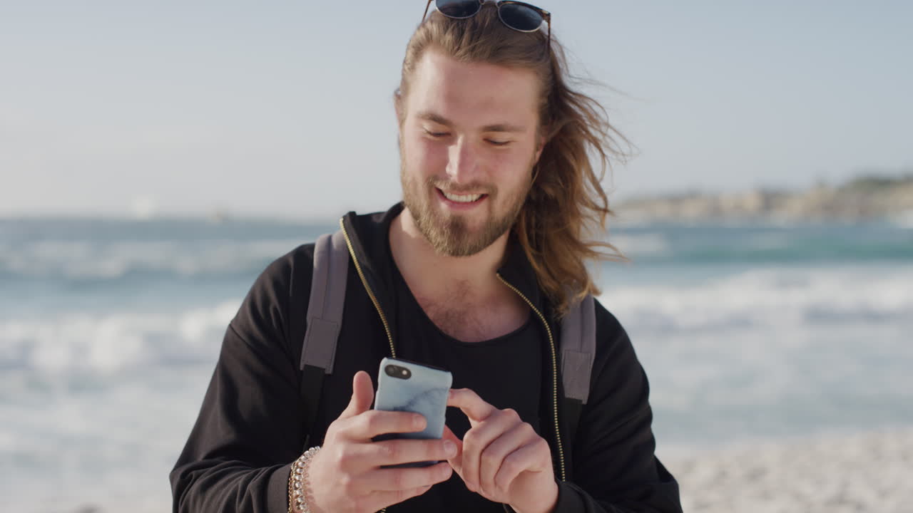 portrait of attractive young man enjoying texting browsing using smartphone feeling connected on summer ocean seaside beach