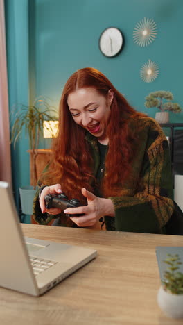 excited caucasian woman playing video game on laptop computer spending leisure time at home office