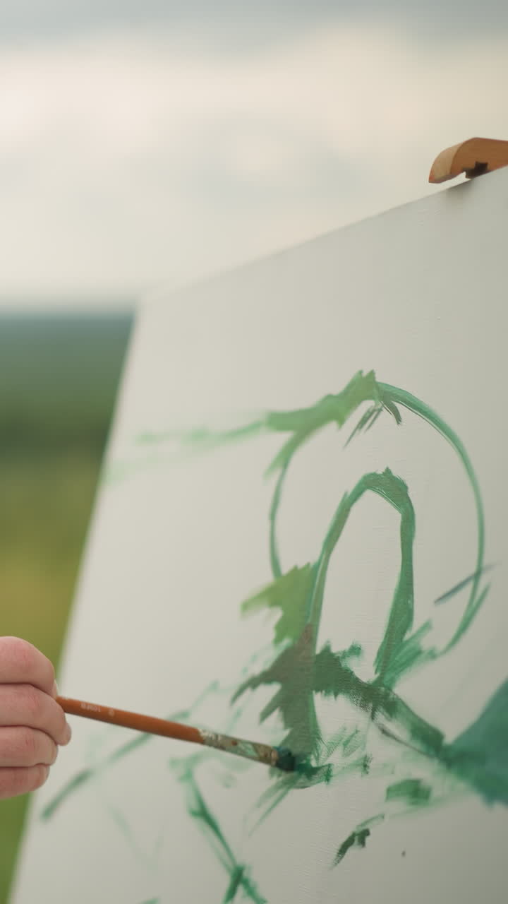 A dedicated artist, dressed in a checkered shirt. He holds a paint palette in one hand and a brush in the other as he gently applies green paint to a large white canvas