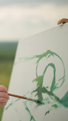 a dedicated artist, dressed in a checkered shirt. he holds a paint palette in one hand and a brush in the other as he gently applies green paint to a large white canvas