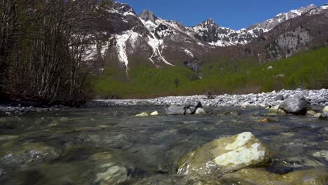 clean water streaming through stones on riverbed with high alps mountain in background