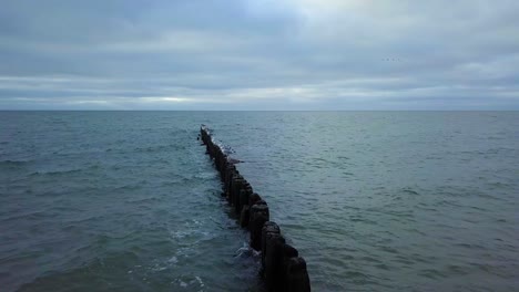 establishing aerial view of baltic sea coast on a overcast day, old wooden pier, white sand beach, low waves crushing against the coast, climate changes, wide angle drone shot moving forward