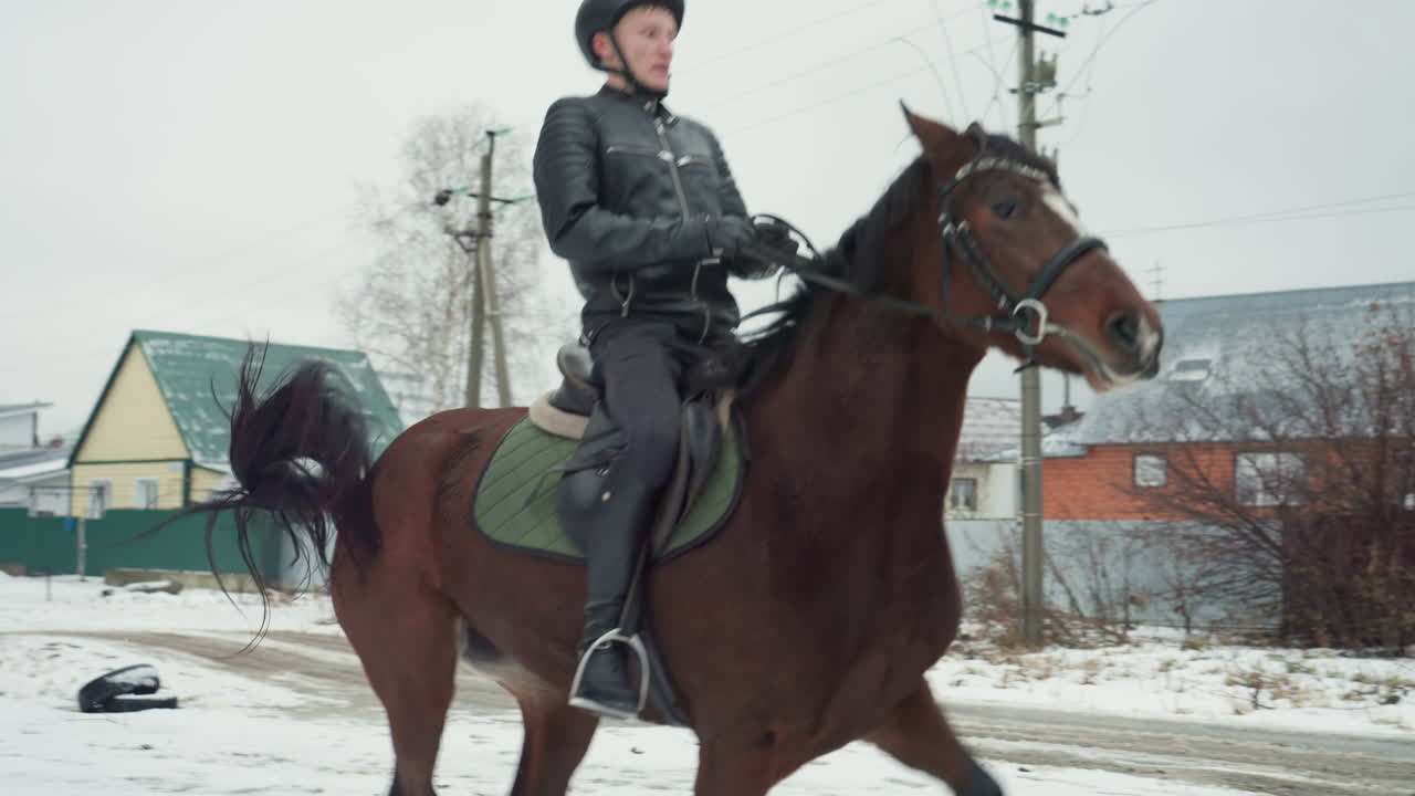 Кавказский конный патруль на коричневой лошади рысью движется по заснеженной обочине, в поле зрения крыши деревни и столбы электропередач, устойчивая осанка, видно патрульное снаряжение и седло, тихое зимнее утро, наполненное бдительностью.