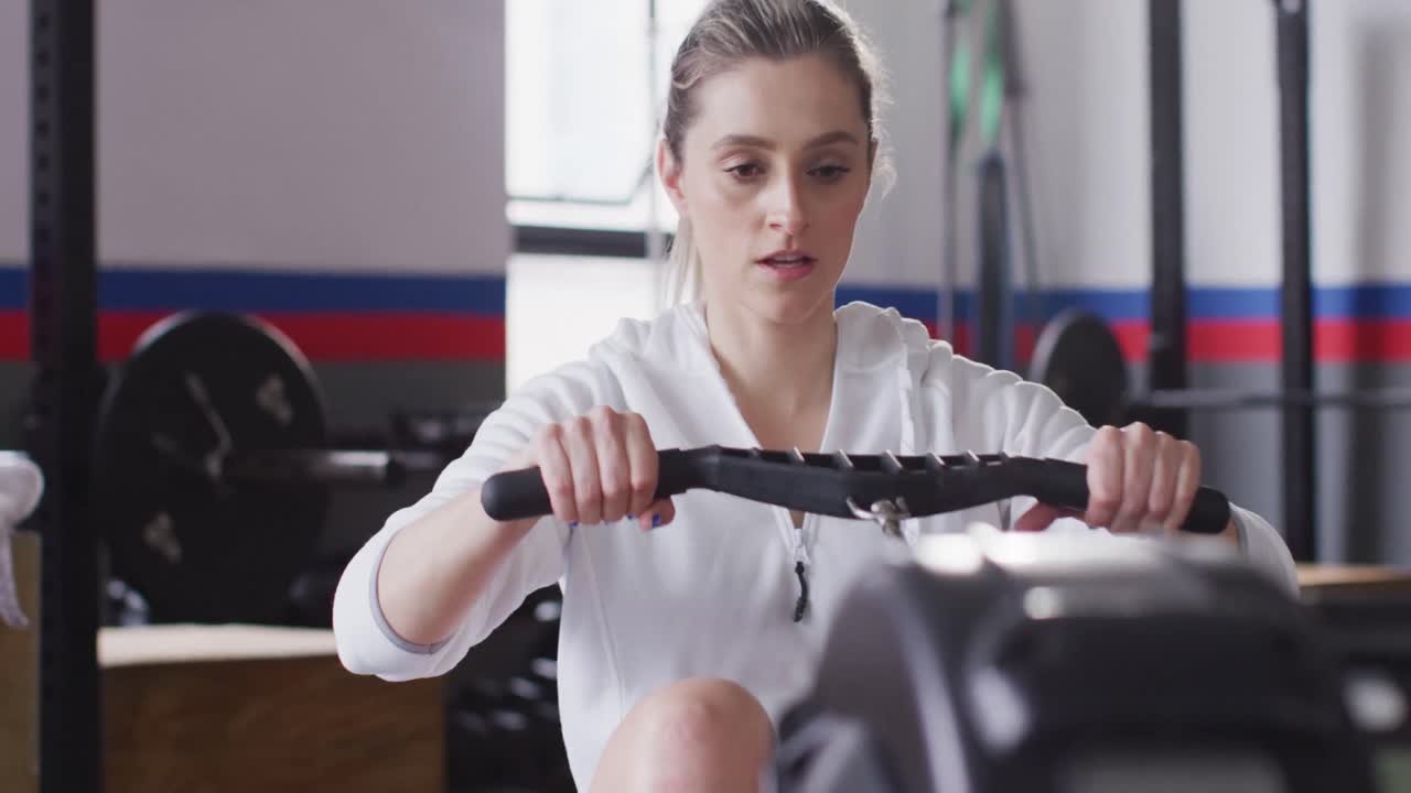 Video of determined caucasian woman using rowing machine working out at gym