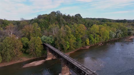 old wooden bridge over tranquil river in forest landscape of usa. sunset time in autumn season. descend drone shot.