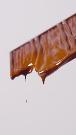 video vertical de primer plano de una barra de chocolate derretida contra un fondo blanco con espacio para copiar