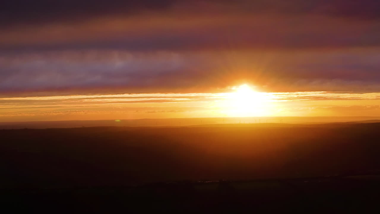 Beautiful sunset over dark landscape with warm, hazy lighting with deep purple clouds creating magical golden hour. Perfect for holiday marketing, winter travel, and seasonal transitions