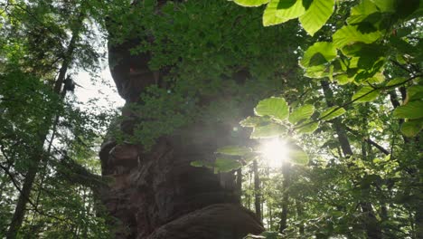 Low-Angle-Aufnahme-Einer-Großen-Felsformation-Mit-Sonnenlicht,-Das-Auf-Das-Unterholz-Scheint