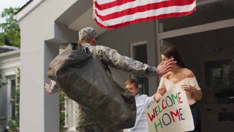 Happy-caucasian-male-soldier-greeting-son-and-wife-with-welcome-home-sign-outside-their-house