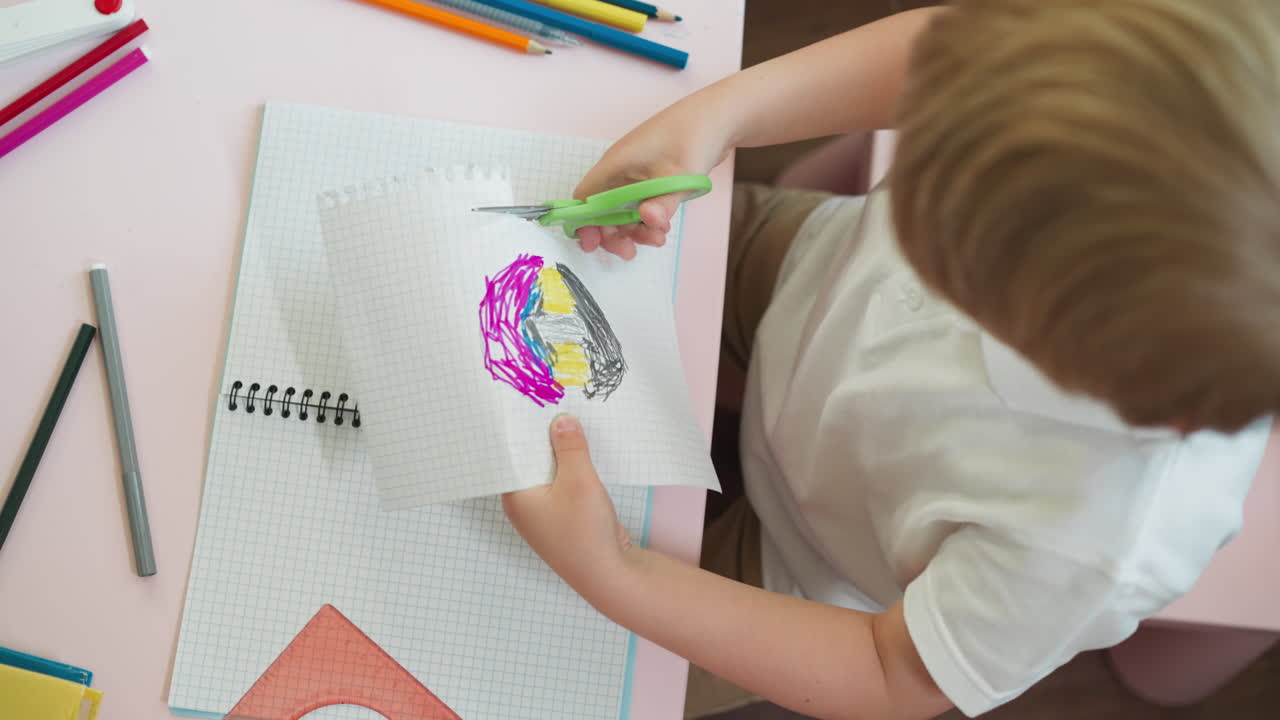 ребёнок режет перфорированный край страницы эскизной книги с картинкой