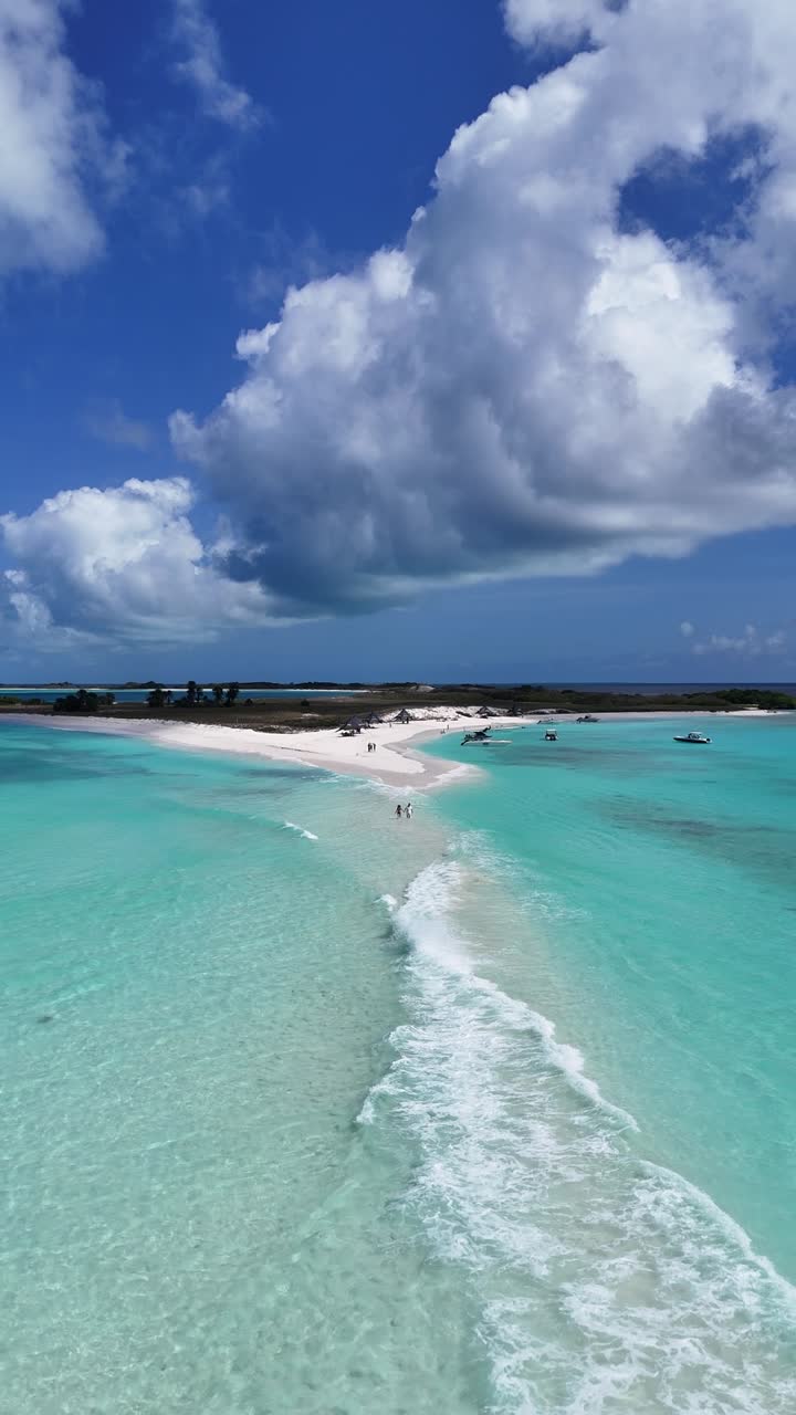 Zoom aereo verticale su una coppia che si tiene per mano mentre cammina sulla lingua di sabbia Paso de Moisés a Cayo de Agua, Arcipelago Los Roques, Venezuela; spiaggia romantica di un'isola tropicale caraibica.