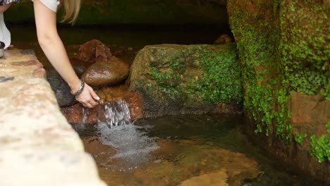 mulher bebe água natural de um pequeno riacho saindo de uma caverna