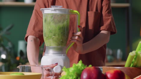 woman making green smoothie in blender at home