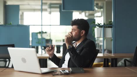 portrait-of-a-handsome,-stylish-young-man-of-Arab-descent-sitting-in-a-modern-business-center-office-with-a-laptop,-turning-on-music,-and-starting-to-dance-and-sing