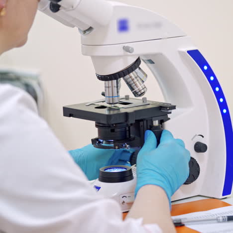 scientist working with modern microscope at laboratory. woman studying samples through the microscope and writes the results. medical, science, doctor, healthcare concept.