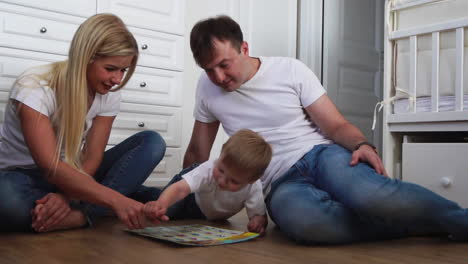 A-family-of-three-in-white-T-shirts-and-blue-jeans-sitting-on-the-floor-of-their-bedroom-playing-with-the-boy-in-intellectual-games.-Slow-motion-shooting-happy-family