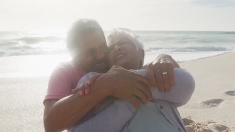 feliz pareja de mayores hispanos sentados y abrazados en la playa al atardecer
