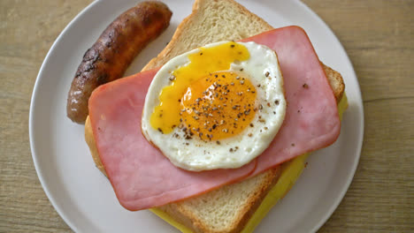 homemade bread toasted cheese topped ham and fried egg with pork sausage for breakfast