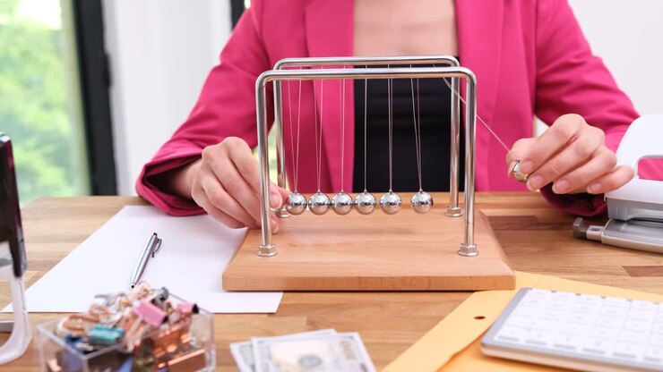 Woman's Hands Playing with Newton's Cradle on Office Desk