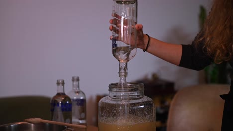 A-stationary-shot-of-a-woman's-hand-pouring-vodka-in-a-glass-pitcher-jar-containing-lemon-and-apple-juice