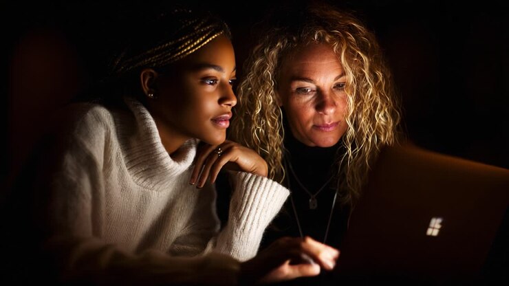 Illuminated Moments: A Young Woman and Her Mentor Collaborate on a Laptop, Sharing Insights in a Warm, Intimate Setting - A Reflection on Learning and Connection
