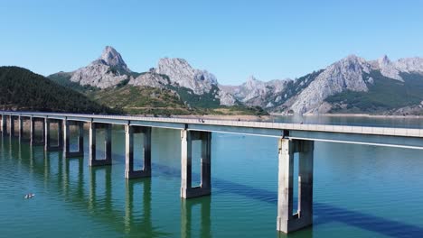 Luftaufnahme-Mit-Drohne-Von-Der-Riaño-Brücke-Im-Vordergrund-Und-Den-Bergen-Im-Hintergrund